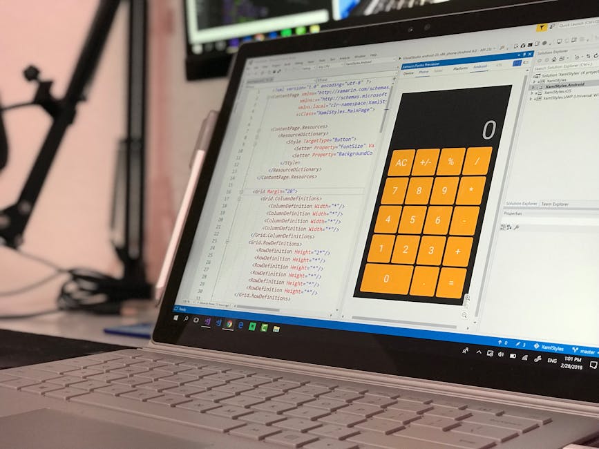 A person working at a desk with a laptop displaying lines of colorful computer code on the screen. The individual, seen from behind, is holding a pen and appears to be reviewing the code. The workspac