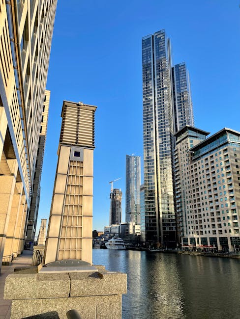 A black and white image of a modern city skyline featuring several high-rise office buildings and skyscrapers with glass facades reflecting light. The tallest building, situated towards the left, has